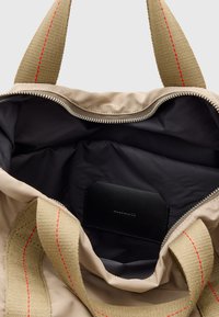 Interior de bolsa beige con forro negro, cierre de plata y dos asas beige con costura roja. Incluye una etiqueta de cuero negro.