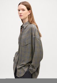 Camicia a quadri grigia con righe gialle e bianche, design con bottoni, tasche sul petto e maniche lunghe. Tessuto morbido e vestibilità rilassata.