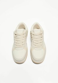 Sneakers w kolorze kremowym, z górną częścią ze gładkiej skóry, okrągłym noskiem, perforowanymi detalami i płaskimi sznurówkami. Gumowa podeszwa stanowi kontrast.