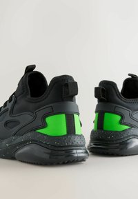 Zwarte sportschoenen met een gestructureerd oppervlak; voorzien van een felgroene accentkleur en een gespikkelde zool; trek-lussen aan de hiel.
