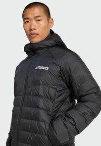 Black puffer jacket with a high collar, quilted design, and zippered front. Features TERREX logo in white on the chest.