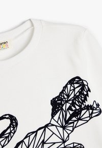 Sweatshirt en coton blanc avec un design géométrique de dinosaure noir sur le devant, doté d'un col rond côtelé et d'une texture lisse.