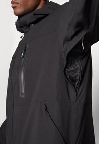 Black waterproof jacket with a hood, featuring a zippered chest pocket and mesh underarm ventilation. Smooth fabric with minimalist design.