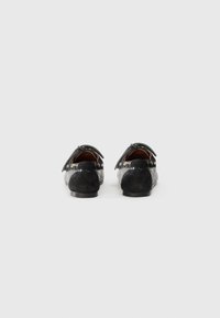 Mocasines negros con un acabado texturizado, que presentan una combinación de ante y material tejido. Lazo decorativo en cada zapato.