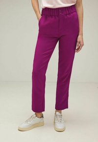 Fuchsia, hög midja byxor med en slät textur, som har två knappar och en avsmalnande ben, i kombination med vita sneakers.