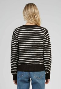 Un pull en rayures marron et crème avec un col rond, des poignets et un ourlet côtelés ; texture douce ; associé à un jean bleu.