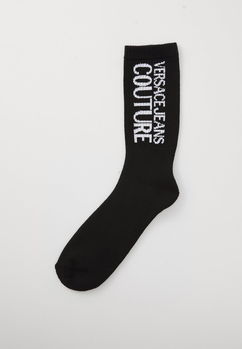 Μαύρη κάλτσα crew με λευκό κείμενο "Versace Jeans Couture" στην ριμπ ώρι του τμήματος, σε απλή φόντο.