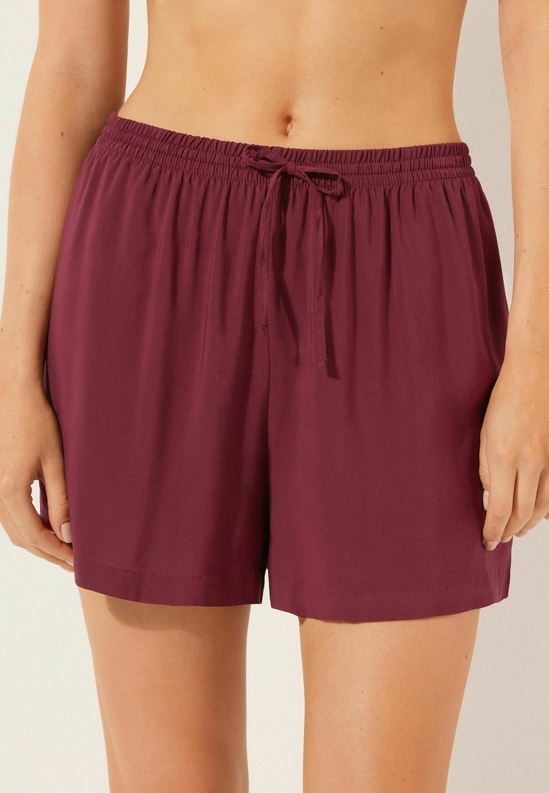 Pantalones cortos ligeros burdeos con cintura elástica y cierre de lazo. Textura suave, corte relajado y longitud hasta la mitad del muslo.