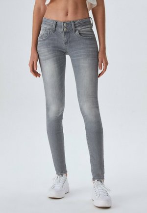 Slim fit grå jeans med dobbelte knapper, iført hvide sneakers på en stående person.