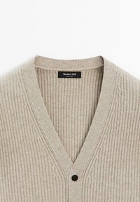 Beige geribbelde brei cardigan met een V-hals en één zwarte knop, met het label "Massimo Dutti" aan de binnenkant.