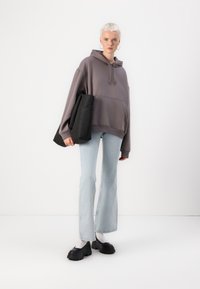 Oversized grå hettegenser med frontlomme, sammen med lyseblå flagrende jeans og kraftige svarte slip-on sko. Svart veske holdt under armen.