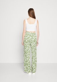 Bílý crop top v kombinaci s širokými kalhotami s květinovým vzorem v zelené barvě, které mají elastický pas. Hladká tkanina s jemnou strukturou.