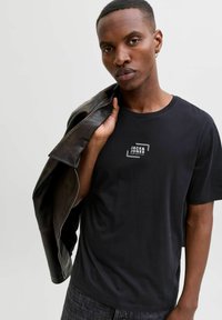 Czarny bawełniany t-shirt z okrągłym dekoltem, z białym prostokątnym logo. Noszony pod ciemną skórzaną kurtką. Gładka faktura, casualowe dopasowanie.
