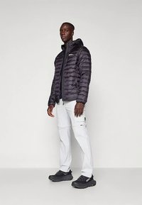 Black puffer jacket with vertical seams, zippered front, and hood, worn over a black base layer and white cargo pants, paired with black shoes.