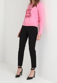 Felpa rosa con scritta rossa "TUTTE LE RAGAZZE DAVANTI", abbinata a pantaloni neri aderenti e tacchi neri alla caviglia.