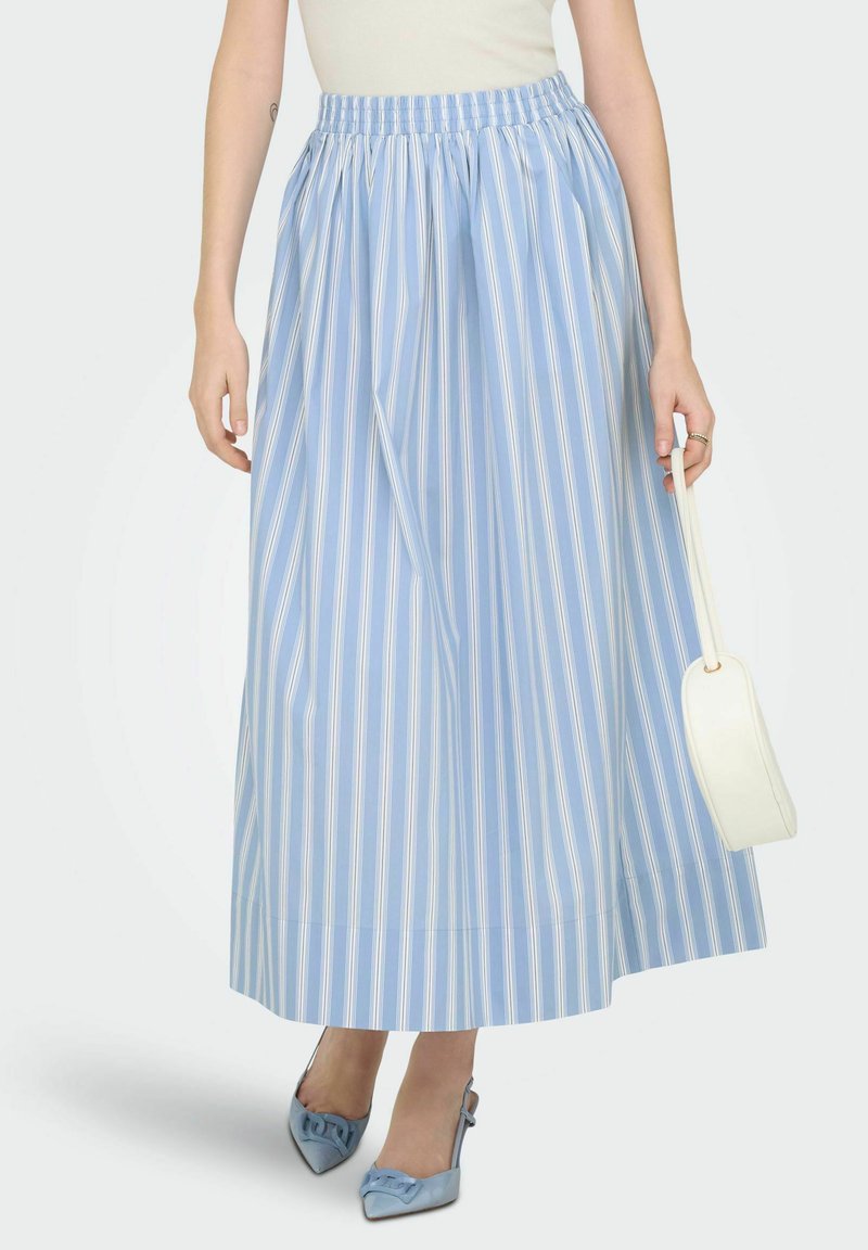 Απαλή μπλε ριγέ μακριά φούστα με ελαστική μέση, λεία υφή, φτάνει μέχρι τους αστραγάλους, συνδυασμένη με λευκή τσάντα και μπλε ψηλές γόβες.