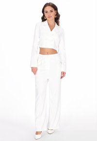 Sacou alb scurt, cu butoni dubli, asortat cu pantaloni albi cu talie înaltă. Textură netedă și potrivire ajustată pe toată lungimea.