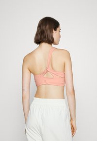 Bralette em tom pêssego com um design de costas recortadas. Feito de tecido macio, com detalhe de alça torcida, textura suave e estética simples.
