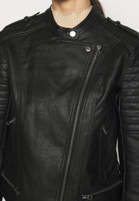 Giacca di pelle nera con una finitura texturizzata, cerniera asimmetrica, dettagli a costine sulle spalle e tasche laterali con zip.