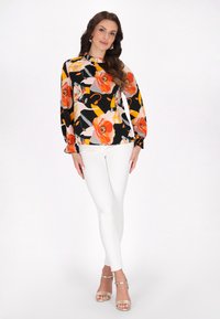 Blommig blus i svart, med orange och rosa blommor, långa ärmar och en volangkrage; matchas med vita figursydda byxor.