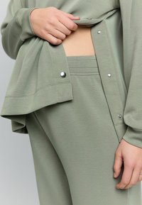 Svetlozelená mikina s patentmi, položená na zodpovedajúcich nohaviciach s úzkym pásom a textúrovanou látkou. Mäkkučký, ležérny outfit.