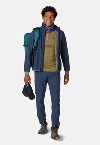 Die Outdoor-Bekleidung besteht aus einer marineblauen Jacke, einem olivfarbenen Hemd und passenden Hosen. Ein blauer Rucksack und grüne Stiefel mit orangefarbenen Akzenten runden den Look ab.