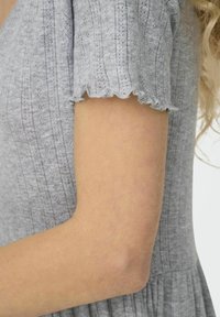 Grå, texturerad klänning med korta, volangärm. Tyget har ränder och subtila detaljer, vilket framhäver en skräddarsydd överdel och en flödande kjol.