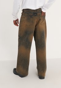 Hnědé džíny s vybledlým modrým vzorem. Mají volný střih, zadní kapsy a široký pas. Na lemu je texturovaný povrch.