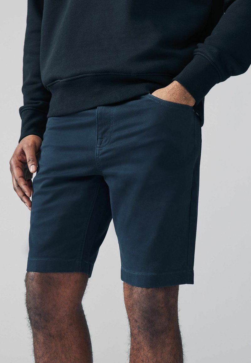 Shorts bleu marine en tissu léger, dotés de poches latérales, d'une coupe droite et d'un léger éclat à la surface.