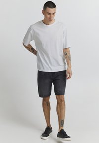 White cotton short-sleeve t-shirt paired with dark denim shorts. The shorts are knee-length and have a casual fit. Black sneakers complete the look.