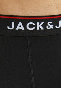 Mustat bokserihousut, joissa on pehmeä kuminauha vyötäröllä, jossa lukee valkoisella tekstillä "JACK & J" ja punainen korostusnauha ylhäällä.