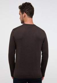 Dunkelbrauner Pullover mit langen Ärmeln und Rundhalsausschnitt, glatter Textur und gerippten Bündchen. Minimalistisches Design ohne sichtbare Muster oder Beschläge.