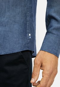 Donkerblauwe linnen shirt met een gestructureerde afwerking, voorzien van een zijsplit en een klein wit-blauw accentlabel bij de zoom.