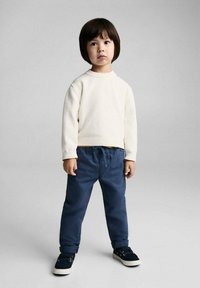 Child wearing a light cream sweater and navy blue elastic waist pants, paired with dark blue sneakers. Simple design, casual fit.
