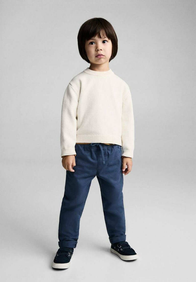 Child wearing a light cream sweater and navy blue elastic waist pants, paired with dark blue sneakers. Simple design, casual fit.