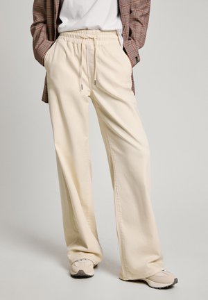 Beige wide-leg trousers made of soft fabric, featuring an elastic waistband with drawstring. Paired with light sneakers and a plaid shirt.