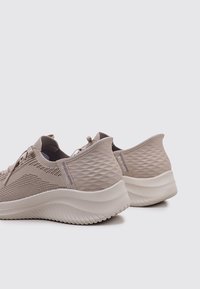 Scarpe da ginnastica beige con tomaia in mesh testurizzato, ammortizzazione morbida e suola flessibile; presenta un motivo a diamante sul pannello posteriore.