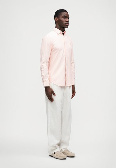 Jasnoróżowa, w paski, koszula na guziki z bawełny, w połączeniu z luźnymi, białymi spodniami z lnu i szarymi butami na slip-on.