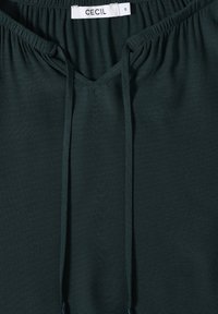 Top verde scuro con scollatura a V, orlo elastico arricciato e dettagli con cordoncino. Realizzato in tessuto morbido e leggero. L'etichetta riporta "CECIL" taglia "S."