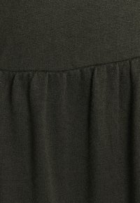 Tessuto di un verde scuro, con una texture che mette in mostra un design arricciato nella parte inferiore. Il materiale sembra lavorato a maglia, con una finitura leggermente ruvida.