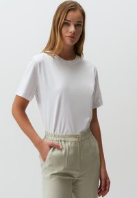 Weißes Baumwoll-T-Shirt mit kurzen Ärmeln und rundem Halsausschnitt, kombiniert mit hellbeigen, hochtaillierten Hosen mit elastischem Bund.