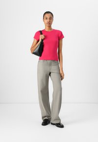 Chemise ajustée rose vif à manches courtes, pantalon large gris clair avec un motif subtil, sac à épaule noir et chaussures noires avec une surface texturée.