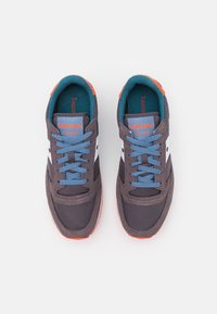 Harmaat kangastennarit, joissa on valkoinen yksityiskohta, vaaleansiniset kengännauhat ja oranssi kantaosa. Sisäpuolella on pehmustettu rakenne ja pohja on kuvioitu tarjoamaan tukea.