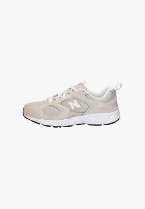 Chaussure de course New Balance beige et grise avec des lacets blancs, des panneaux en maille, et une semelle blanche amortie sur fond blanc.