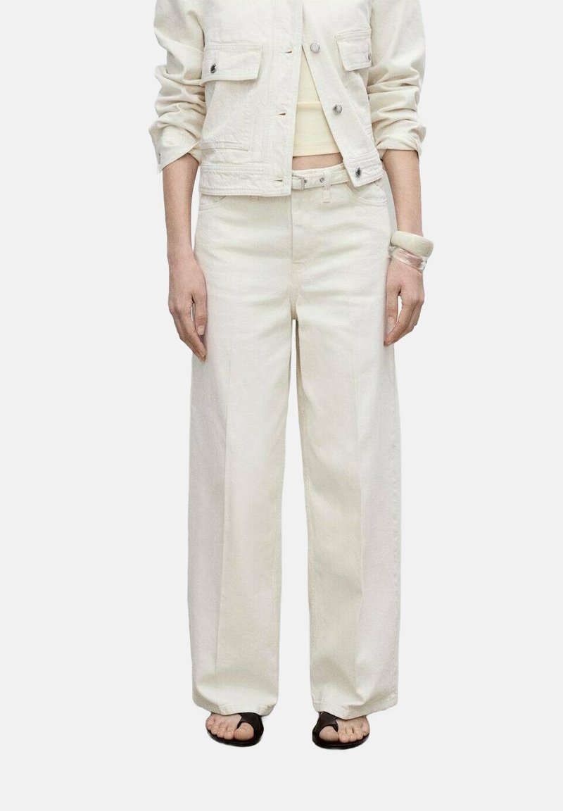 White denim jacket with two chest pockets, paired with loose-fitting white pants. Features a straight cut and worn with black sandals.