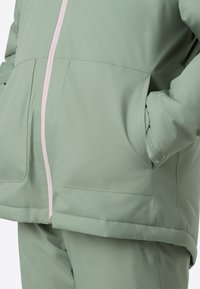 Φωτεινό πράσινο μπουφάν με λεία υφή, με φερμουάρ μπροστά σε ροζ χρώμα, πλαϊνές τσέπες και ελαστικά μανίκια.