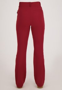Rode slimfit broek met een achterzaknaad, gedragen door een persoon die tegen een effen lichte achtergrond staat.