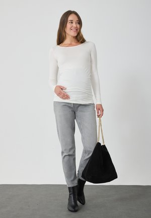 Bluză albă cu mâneci lungi, mulată, blugi gri, botine negre cu toc, ținând o geantă mare din suede neagră cu un mânere din lanț auriu.