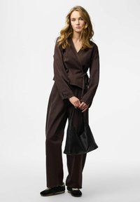 Brun wrap-top kombineret med matchende brune bukser, holder en sort lædertaske. Outfit indeholder lange ærmer og en afslappet pasform.