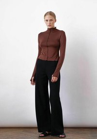 Bruine, lange mouwen, geribbelde top met gerimpelde kraag, gecombineerd met hoge taille, wijde zwarte broek en zwarte schuifsandalen.